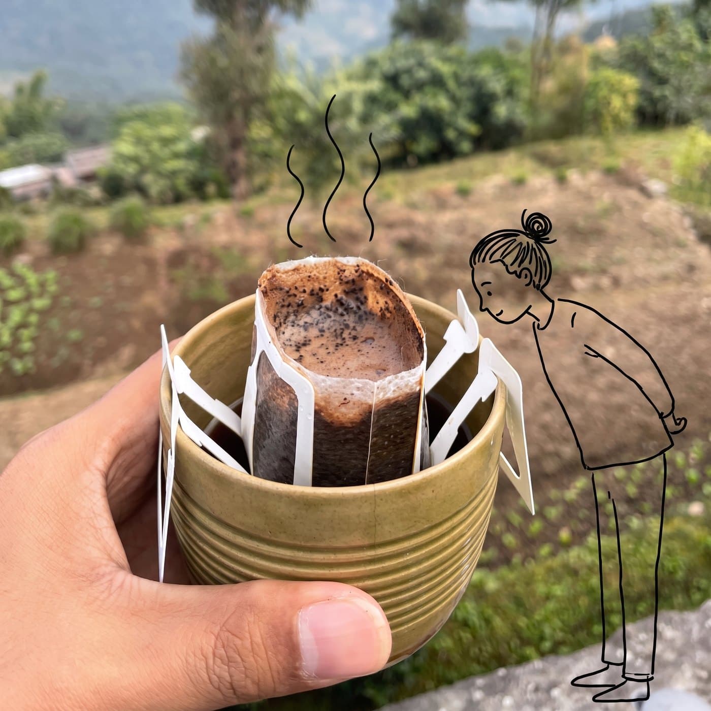 A hand holding a ceramic cup on the farm in Kavre, with a Cliff Natural Coffee drip sachet hooked over the rim, and a small drawn figure leaning in to smell it